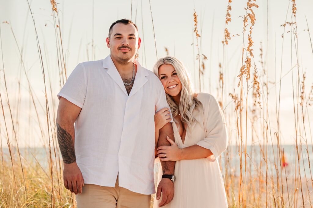Taylor and Grant standing along the sea oats, creating a picturesque scene at Pass-a-Grille Beach during their engagement session.