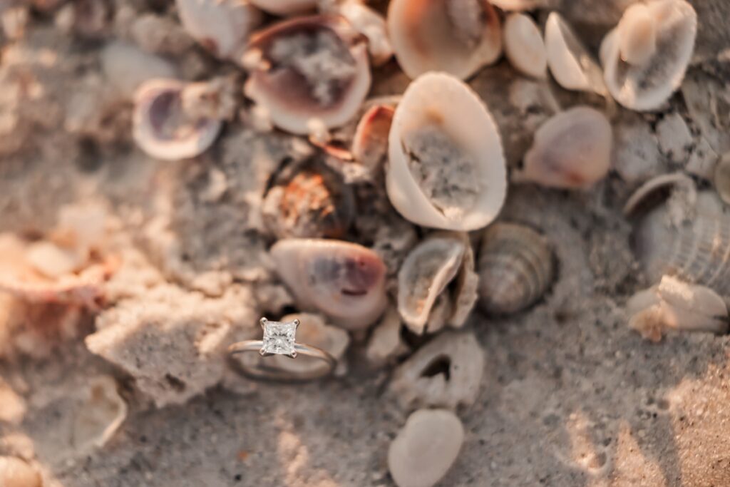 Close up of engagement ring in the sand with shells at Pass-a-Grille Beach.
