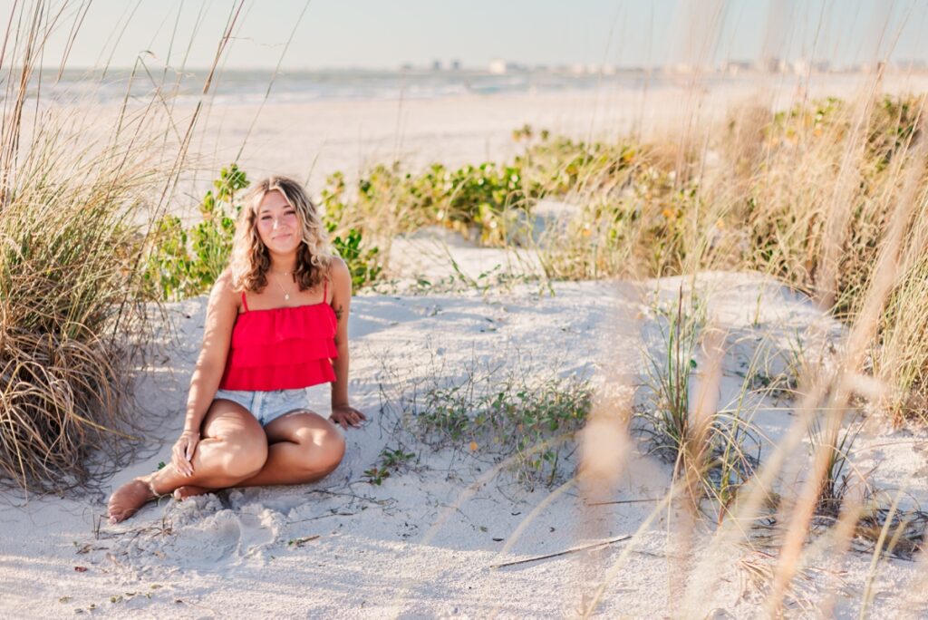 Senior girl in bright top posing on dunes at St. Petersburg Beach.