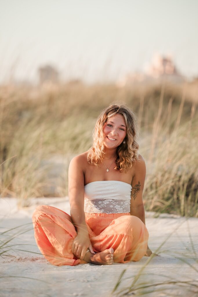 Senior girl in bright pants posing on sand at St. Petersburg Beach.