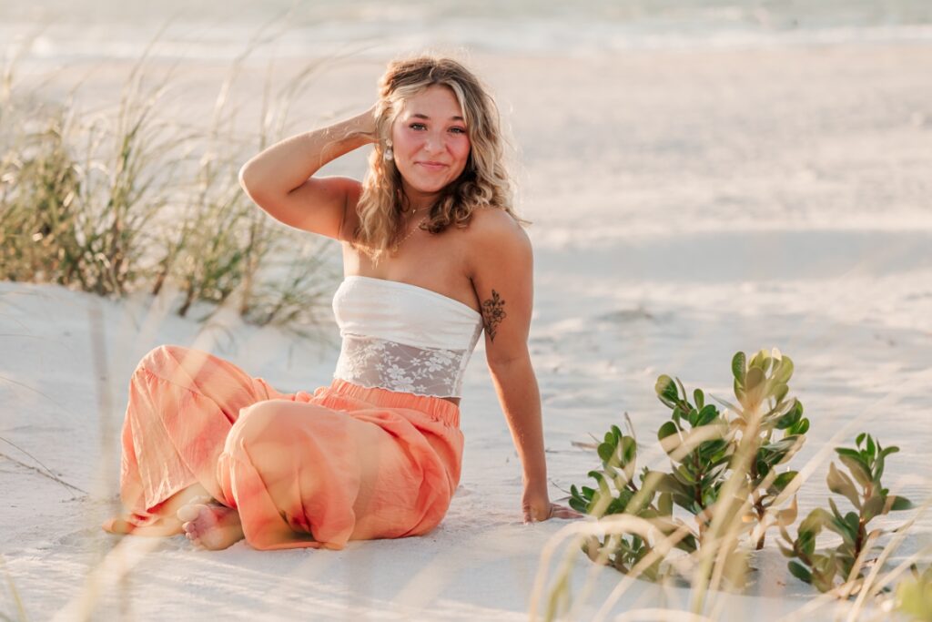 Senior girl in bright pants posing on sand at St. Petersburg Beach, FL.