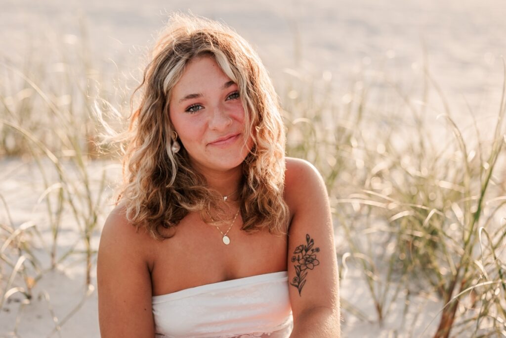 Senior girl in white top posing on dunes at St. Petersburg Beach, FL.