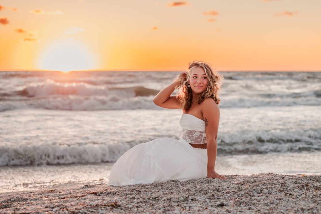 Senior girl in all white posing by the water at sunset in St. Petersburg Beach, Florida.