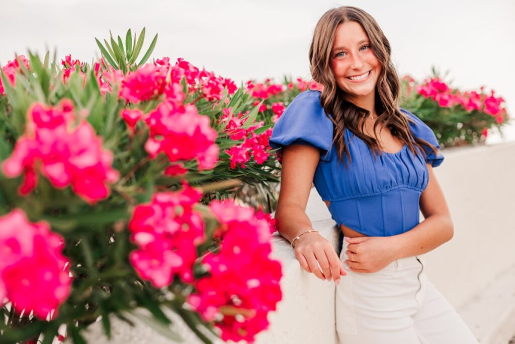 Senior girl posing in blue and white outfit in front of pink tropical flowers.