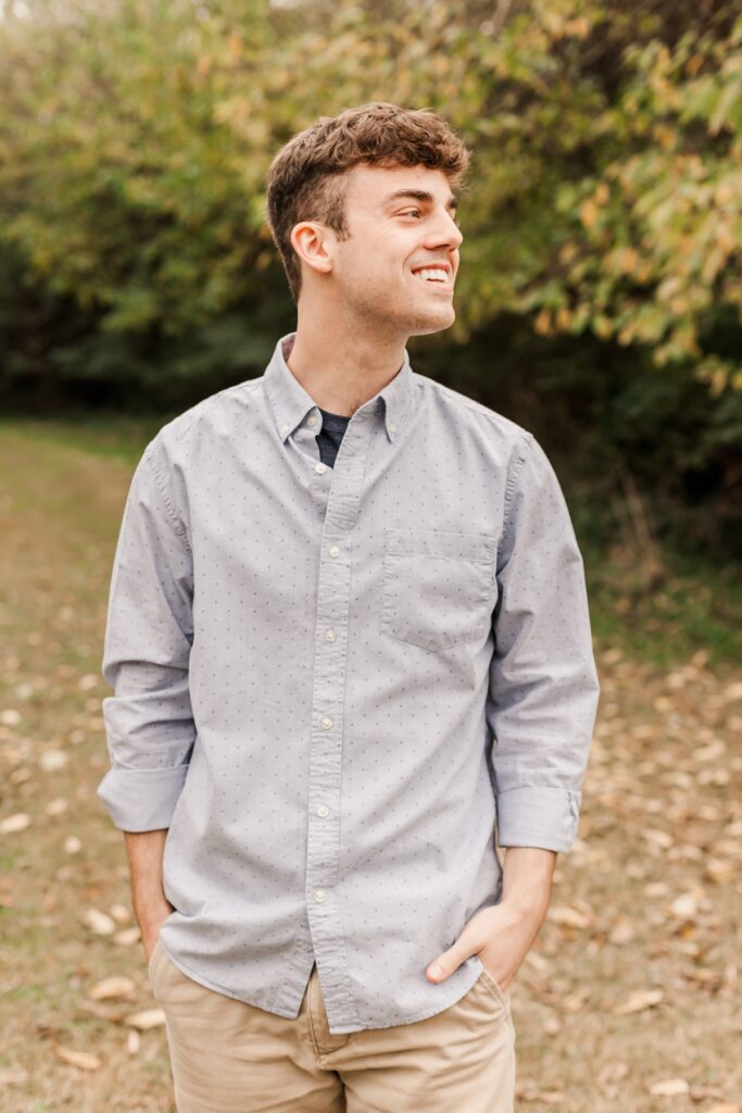 A male graduate standing in front of trees smiling joyfully at the horizon.