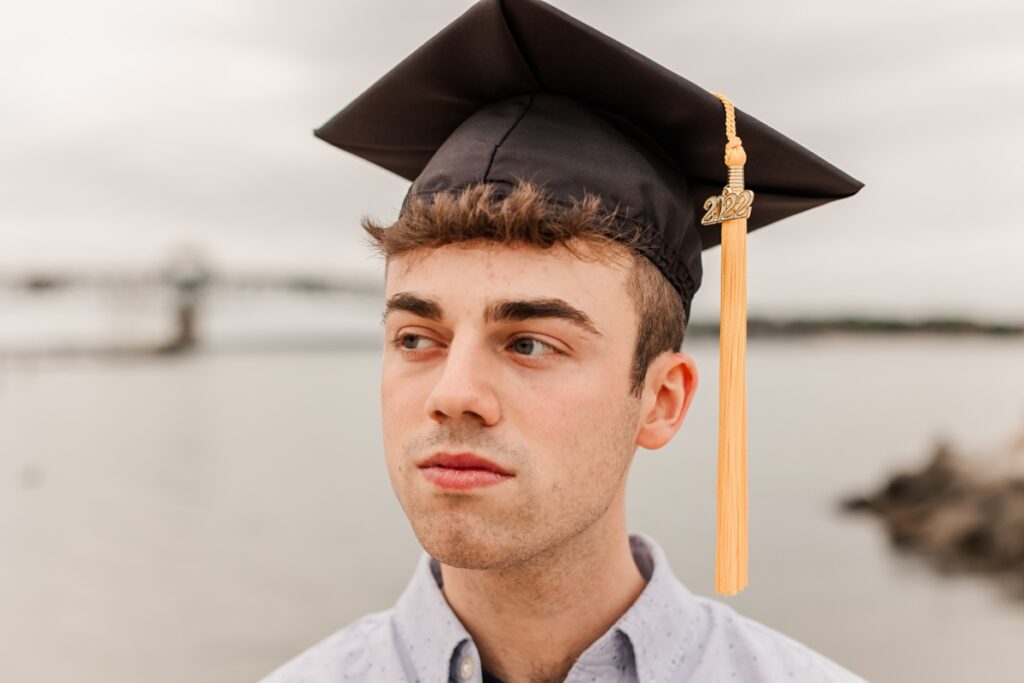 A close-up shot of a male graduate with his cap the beach and ocean softly blurred in the background.