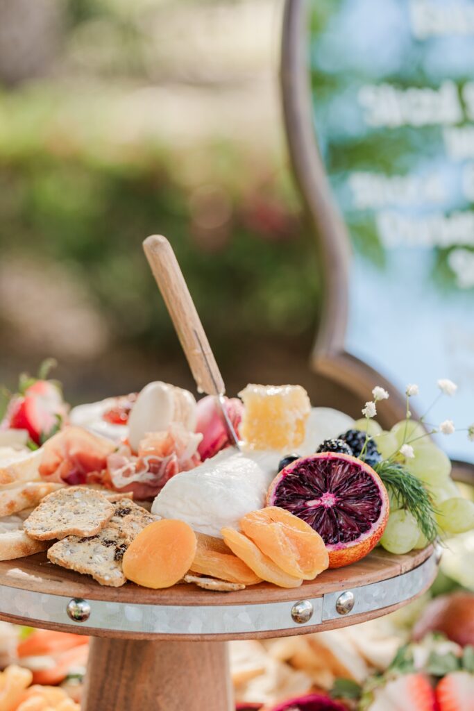 Close-up of artisanal cheeses, salami slices, and fruit arranged on a rustic charcuterie board.