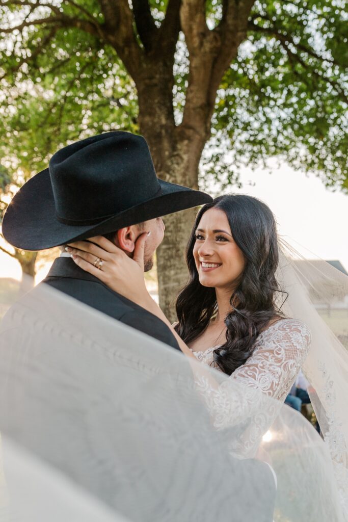 Romantic portrait of newlyweds wrapped together in the bride’s veil during a rustic barn wedding.